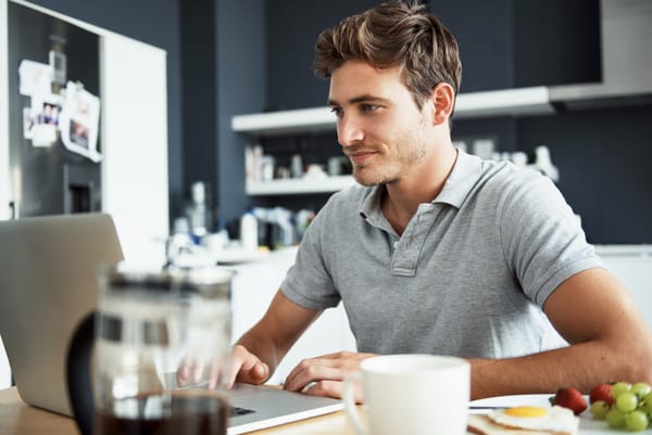 young man focusses intently at the screen of his laptop at the kitchen table